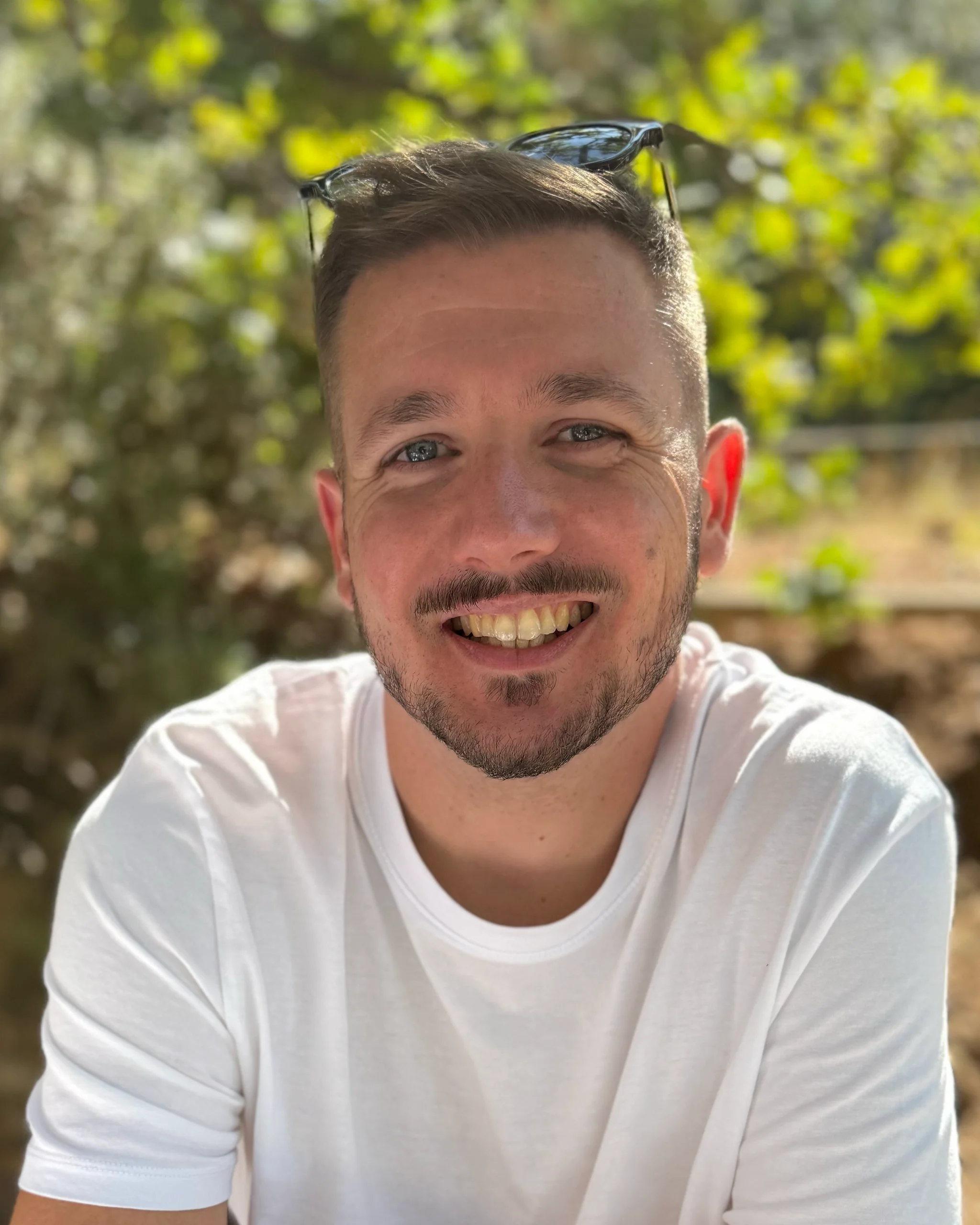 Maxence Rose (pirmax), développeur web à Marseille Maxence Rose sourit face à l’objectif, en t-shirt blanc, des lunettes de soleil relevées sur la tête, en plein air devant de la verdure.